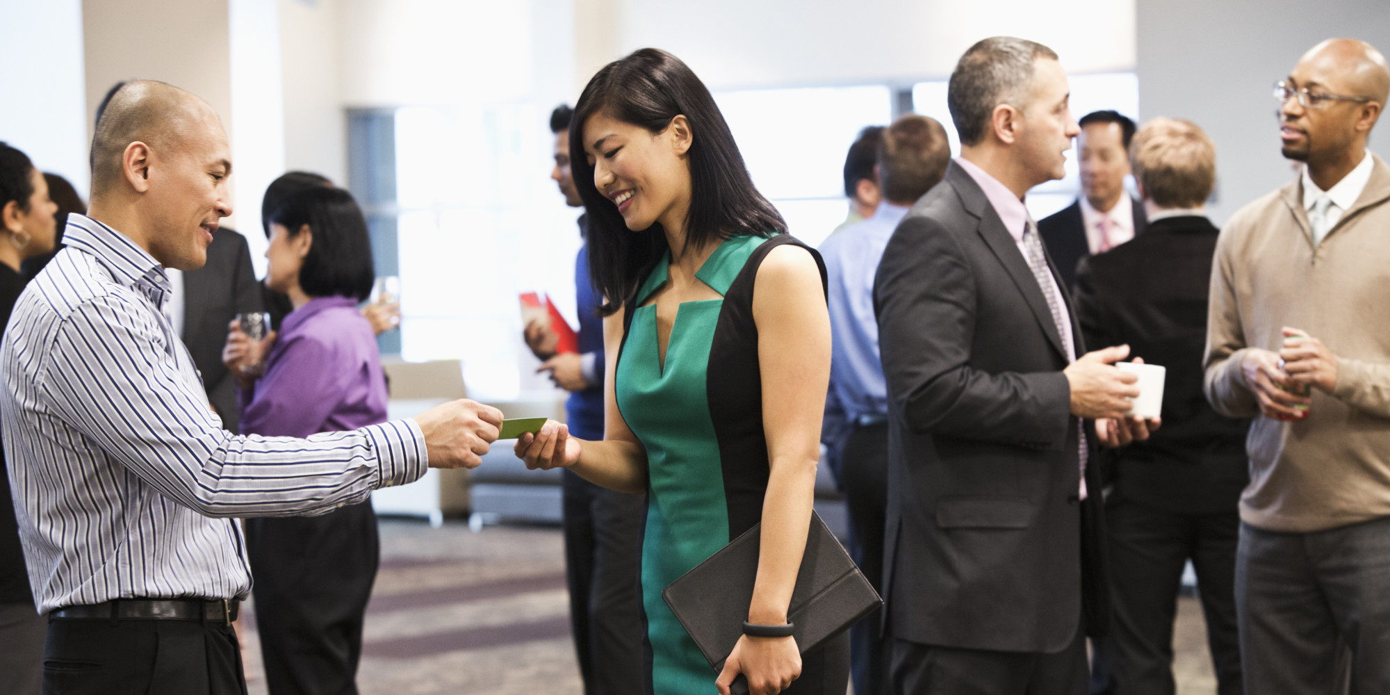 a man giving a card to a woman and other people talking to each other in formal attire