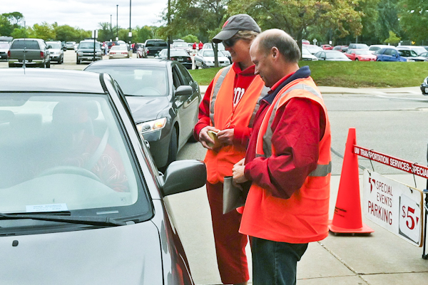 two parking attendants in orange vest talking to the car driver