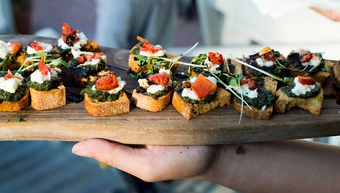 a hand holding a wooden tray of bite size foods