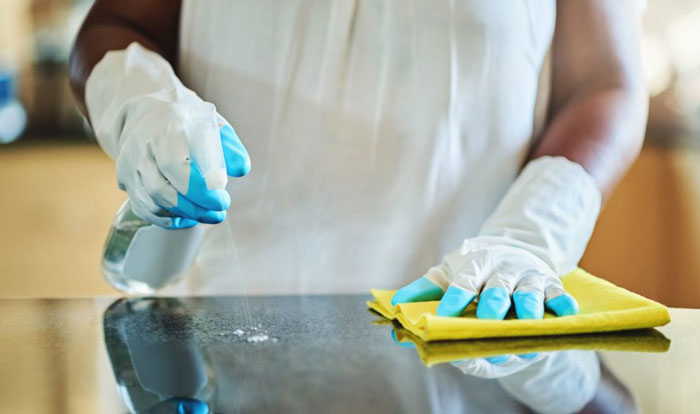 a person wearing gloves sanitizing the table using disinfectant spray and a cleaning cloth