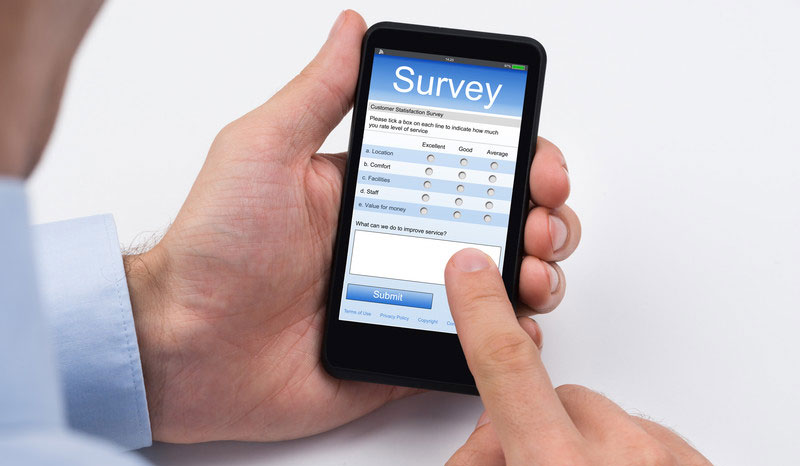 left hand is holding a mobile phone with a survey open on the screen while the right index finger is touching the screen