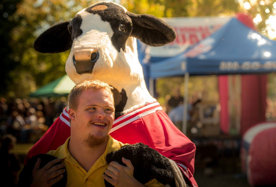 a happy man with down syndrome and a cow mascot behind him