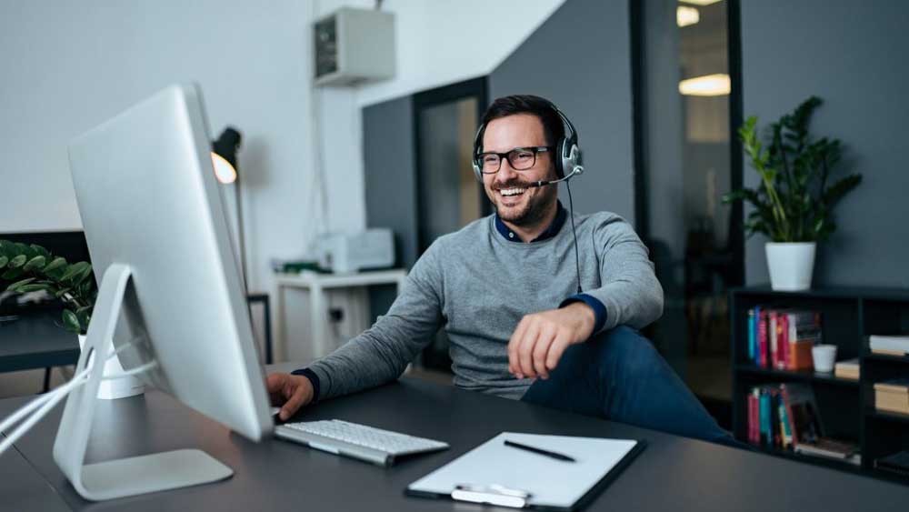 a-man-smiling-with-headphones-on-looking-at-his-computer